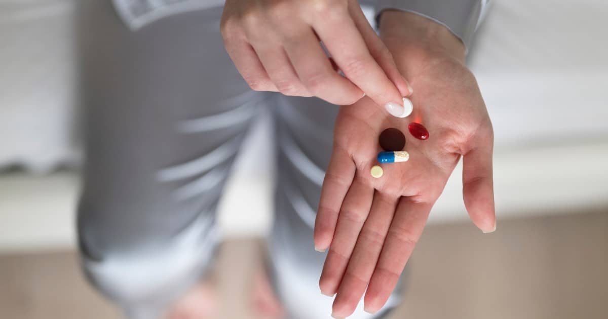 pessoa mostrando medicamentos na mão, incluindo cápsula verde e branca